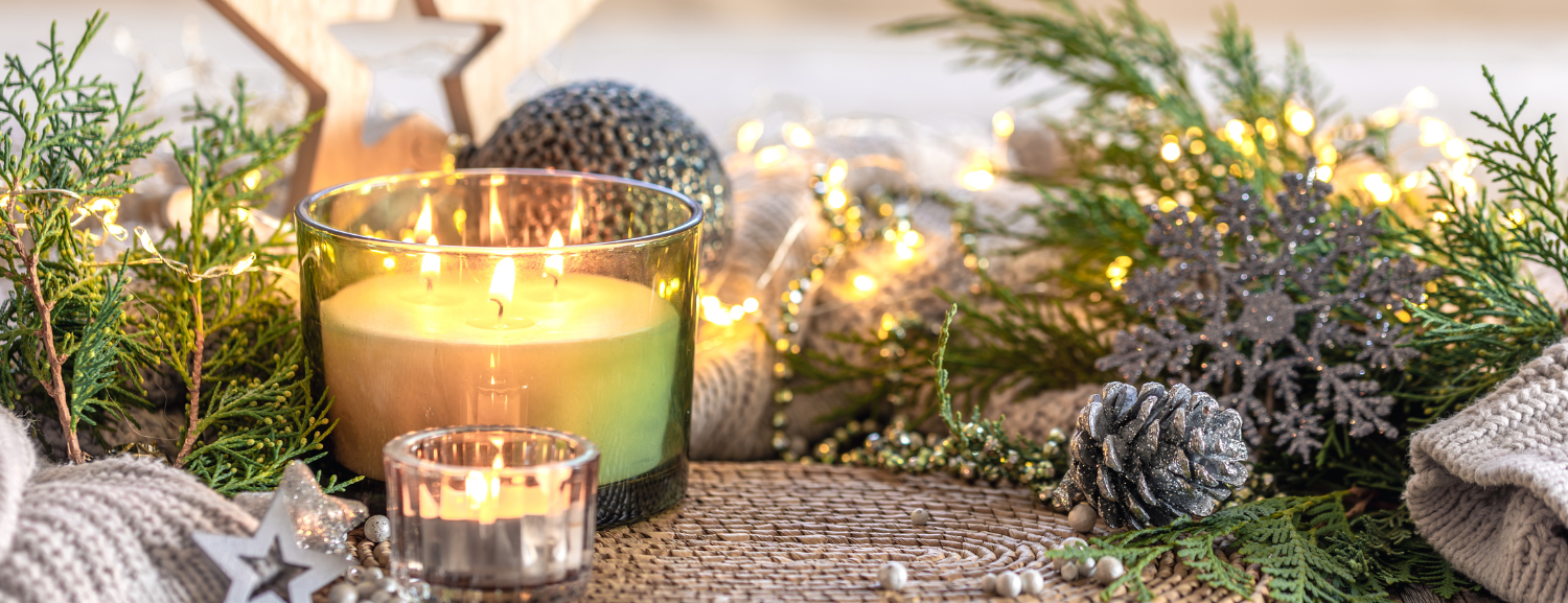 Decorative setting with candles, pine cones, and greenery on a textured surface.